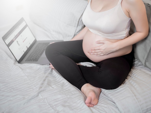 Hermosa mujer embarazada asiática está trabajando con su portátil