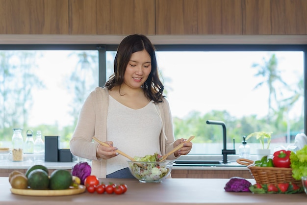 Una hermosa mujer embarazada asiática felizmente preparando una ensalada de verduras orgánica