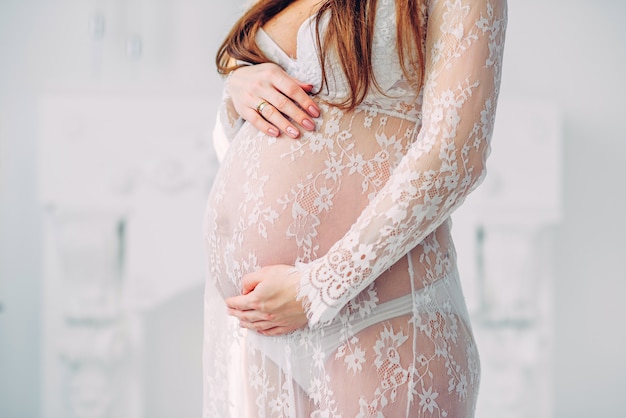 Hermosa mujer embarazada en una bata de encaje blanco sosteniendo el vientre embarazado