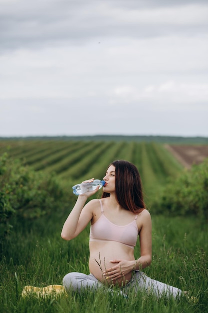 Hermosa mujer embarazada bebiendo agua en las noches de verano después de hacer yoga