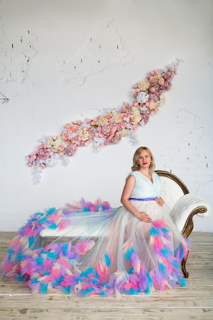 Foto hermosa mujer embarazada con un colorido vestido hinchado está sentada en el sofá copia espacio feliz embarazo