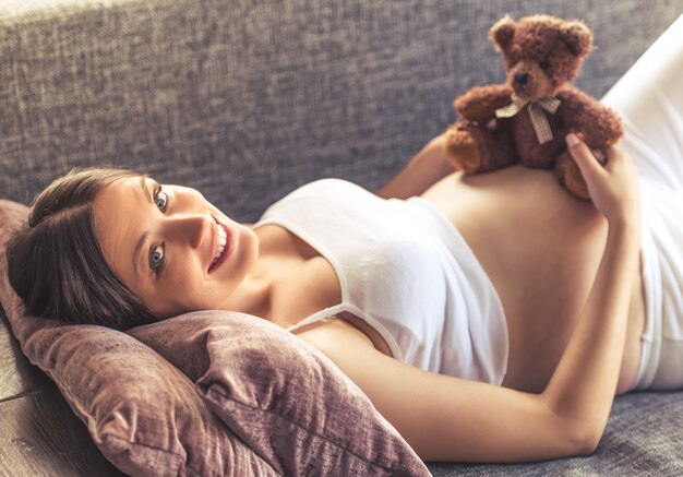 Hermosa mujer embarazada está sosteniendo un oso de peluche.