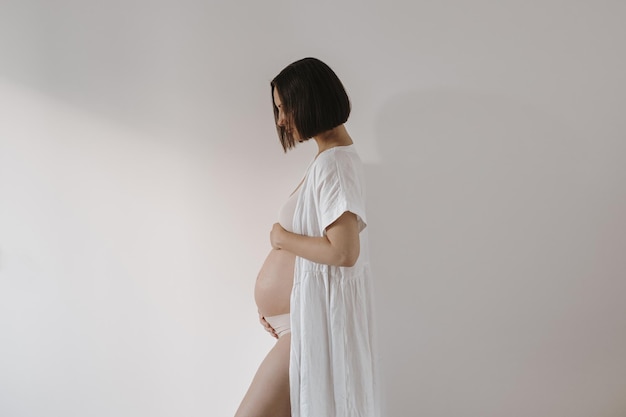 Hermosa mujer embarazada feliz en elegante túnica blanca tocando su barriga Estética elegante embarazo maternidad bebé recién nacido esperando concepto