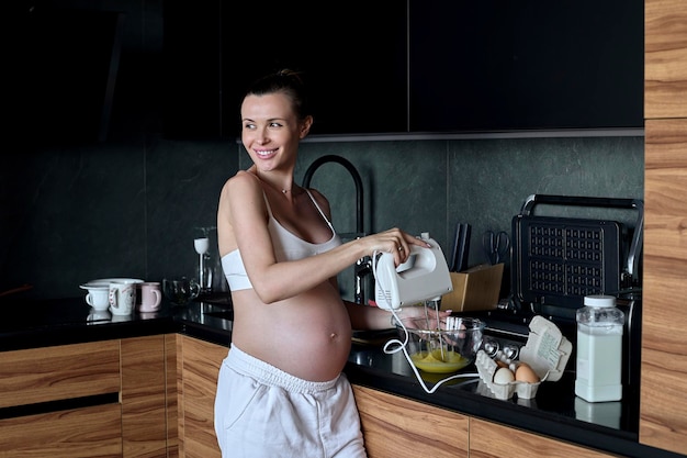Hermosa mujer embarazada haciendo batidos de frutas con licuadora H