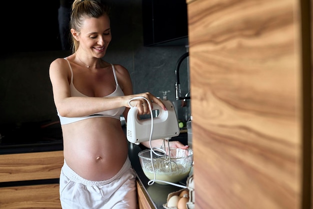 Hermosa mujer embarazada haciendo batidos de frutas con licuadora H