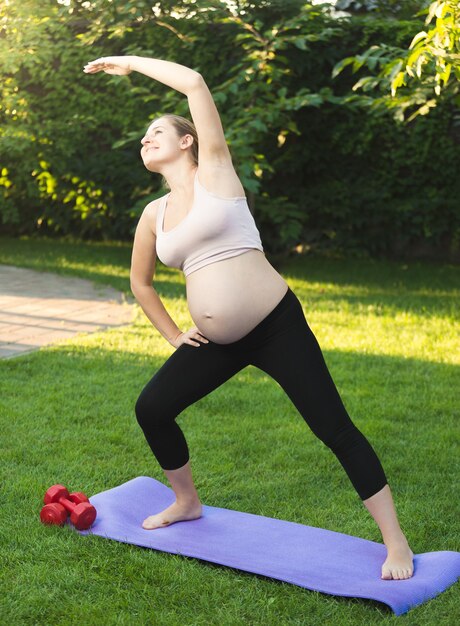 Foto hermosa mujer embarazada haciendo ejercicio sobre la hierba verde en el parque