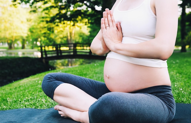 Hermosa mujer embarazada haciendo yoga prenatal en la naturaleza al aire libre