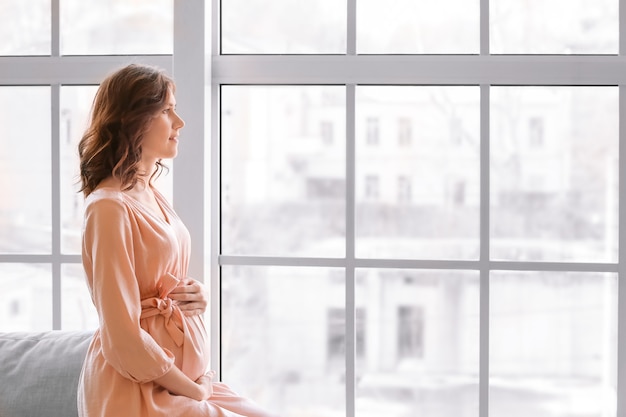 Hermosa mujer embarazada junto a la ventana en casa