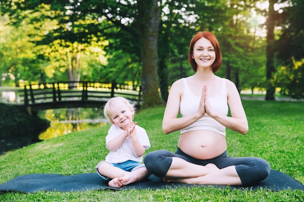 Hermosa mujer embarazada y madre con su lindo hijo pequeño en posición de loto haciendo yoga