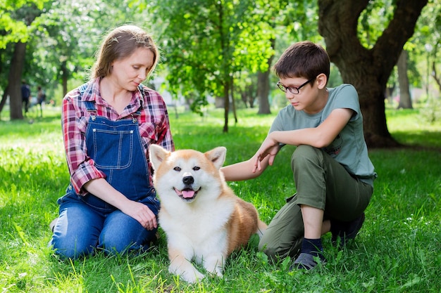 Hermosa mujer embarazada con overoles de mezclilla azul con su hijo y el perro japonés Akita inu en el parque