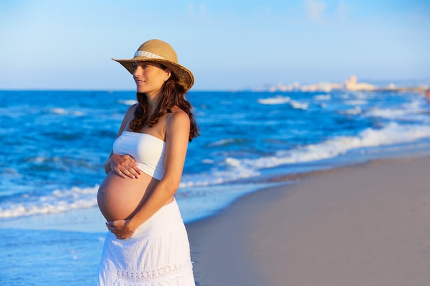 Hermosa mujer embarazada en la playa con sombrero