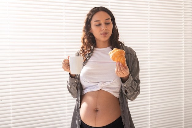 Hermosa mujer embarazada sana bebiendo té y comiendo croissant durante el almuerzo concepto de