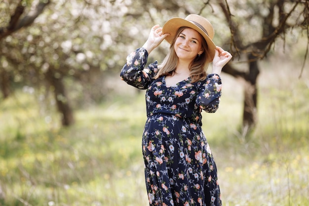 Una hermosa mujer embarazada con un sombrero de paja en el parque de flores de primavera.