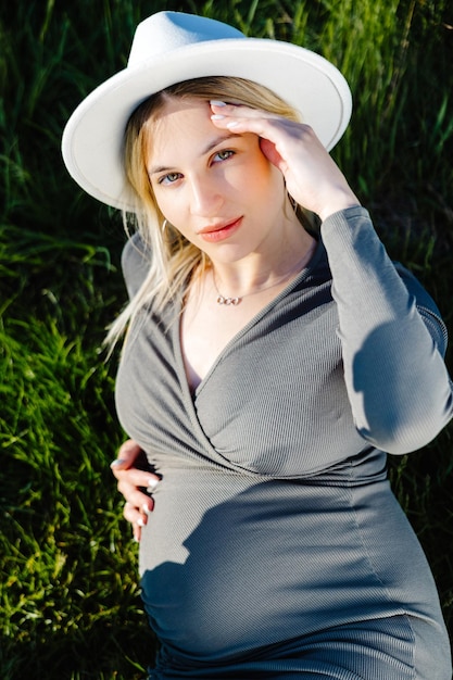 Hermosa mujer embarazada con sombrero y vestido tirado en la hierba