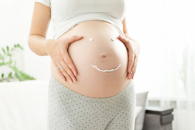 Hermosa mujer embarazada con sonrisa dibujada por crema para estrías en la barriga