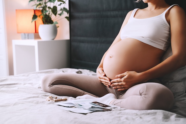 Hermosa mujer embarazada tiene las manos sobre su vientre en el dormitorio en casa