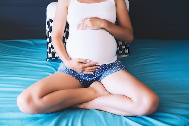 Hermosa mujer embarazada tiene las manos sobre el vientre en el dormitorio en casa