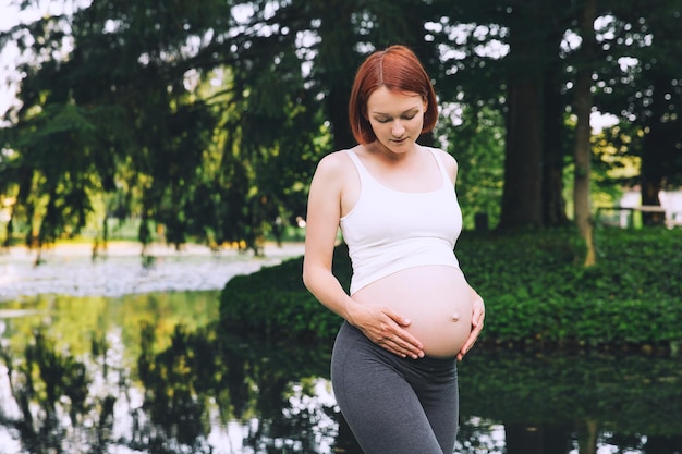 Hermosa mujer embarazada tiene las manos en el vientre al aire libre Conceptos de estilo de vida saludable durante el embarazo