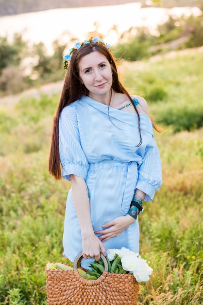 Hermosa mujer embarazada con vestido azul en jardín floreciente