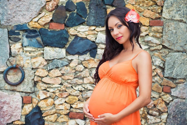 Hermosa mujer embarazada en un vestido naranja en el fondo de la pared de piedra. Antiguo pueblo de Altos de Chavón, República Dominicana