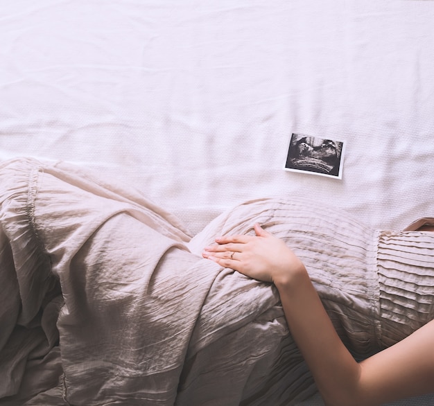 Hermosa mujer embarazada en vestido tomados de la mano sobre el vientre acostado de lado de perfil en la cama