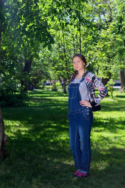 Hermosa mujer en el embarazo temprano en general de mezclilla de pie sobre la hierba verde en el parque