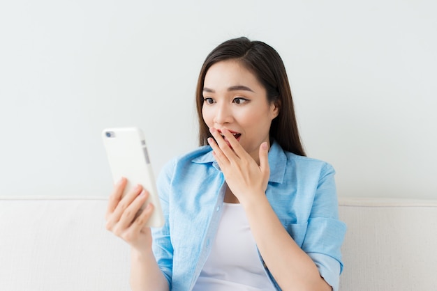 Hermosa mujer emocionada mirando smartphone en casa