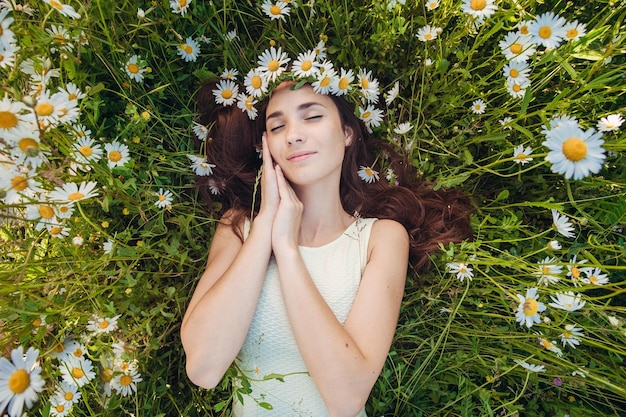 La hermosa mujer se encuentra en el campo de chamomiles Mujer morena feliz despreocupada con cabello largo saludable divirtiéndose al aire libre en el concepto de armonía de la naturaleza