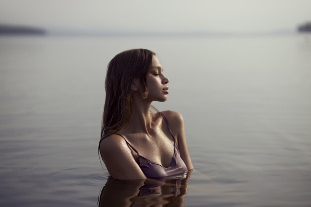Hermosa mujer se encuentra con la puesta de sol sentada en el lago cuerpo perfecto cabello mojado Vacaciones relajarse junto al agua