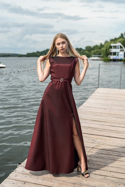 Hermosa mujer se encuentra con vestido largo rojo oscuro en la naturaleza. Concepto de viaje.