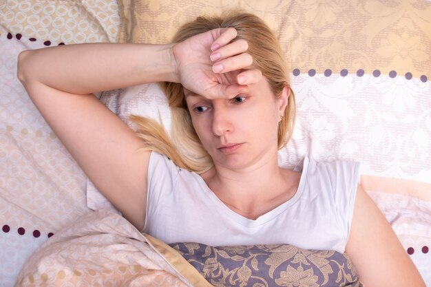 Una hermosa mujer enferma acostada en la cama con dolor de cabeza, migraña y sufrimiento
