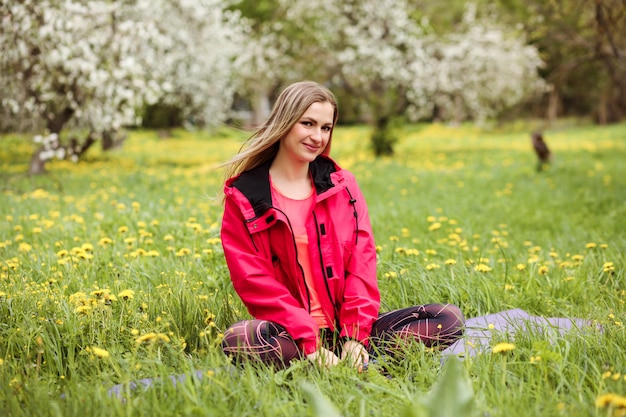 Hermosa mujer es relajarse al aire libre, sentado en la estera en el parque floreciente