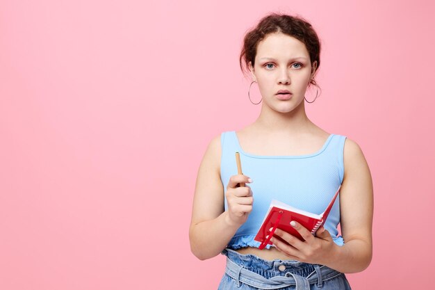 Hermosa mujer escribiendo en un cuaderno rojo con un fondo de color rosa de estudio de pluma inalterado