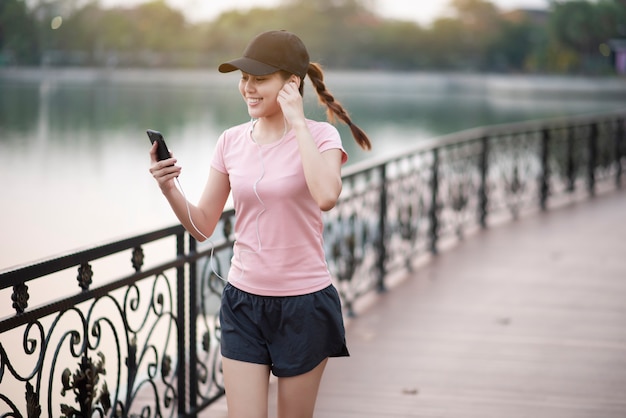 Hermosa mujer está escuchando música y corriendo en el parque