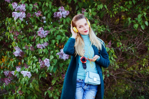 Hermosa mujer está escuchando la música en sus auriculares al aire libre en el parque entre las flores de color lilas.