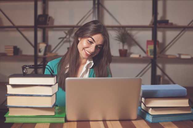 Hermosa mujer está feliz por su exitoso trabajo con una computadora portátil gris y sus libros en la mesa