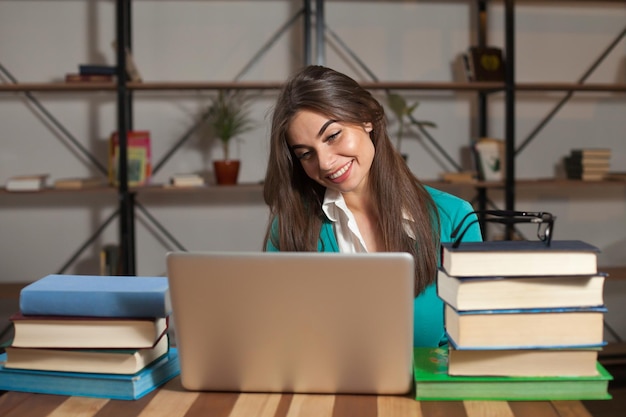 Hermosa mujer está feliz por su exitoso trabajo con una computadora portátil gris y sus libros en la mesa