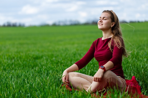 Hermosa mujer está sentada en la hierba y descansando. La niña cerró los ojos y disfrutó del sol. Ella sonríe y disfruta de un día cálido.