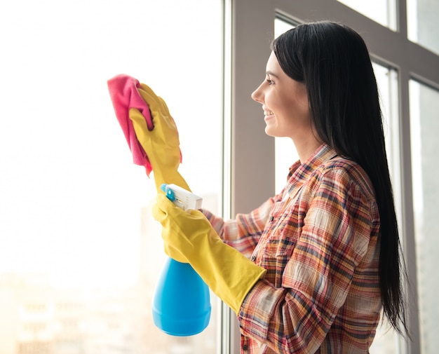 Hermosa mujer está sonriendo mientras limpiaba la ventana en casa