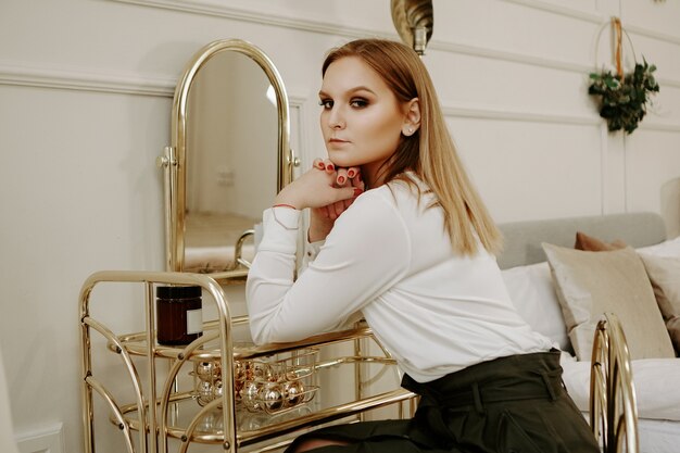 Foto hermosa mujer en una estricta blusa blanca en su habitación cerca de su tocador