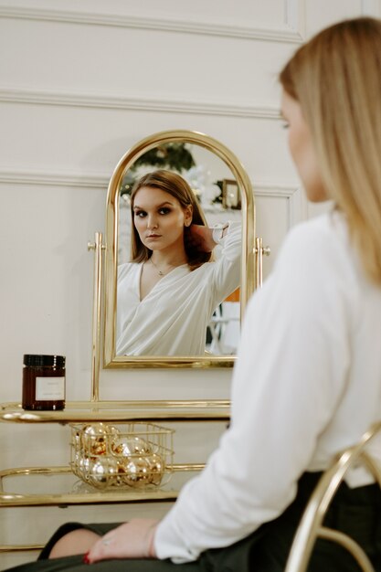 Hermosa mujer en una estricta blusa blanca en su habitación cerca de su tocador