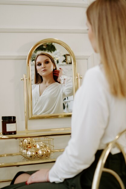 Hermosa mujer en una estricta blusa blanca en su habitación cerca de su tocador