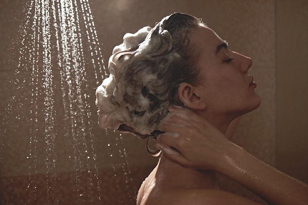 Hermosa mujer europea satisfecha lava el champú del cabello en el baño, se ducha y disfruta, sonriendo
