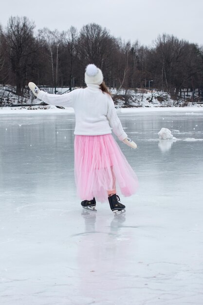 Una hermosa mujer con una falda de tul rosa y un suéter blanco está patinando patinaje artístico en el río