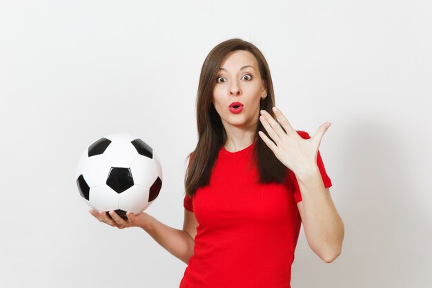 Hermosa mujer feliz alegre joven europea, aficionado al fútbol o jugador en uniforme rojo con balón de fútbol clásico aislado sobre fondo blanco. Deporte, fútbol, salud, concepto de estilo de vida saludable.