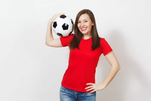 Hermosa mujer feliz alegre joven europea, aficionado al fútbol o jugador en uniforme rojo con balón de fútbol clásico aislado sobre fondo blanco. Deporte, fútbol, salud, concepto de estilo de vida saludable.