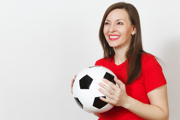 Hermosa mujer feliz alegre joven europea, aficionado al fútbol o jugador en uniforme rojo con balón de fútbol clásico aislado sobre fondo blanco. Deporte, fútbol, salud, concepto de estilo de vida saludable.