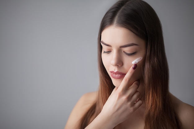 Hermosa mujer feliz aplicando crema cosmética en la cara limpia