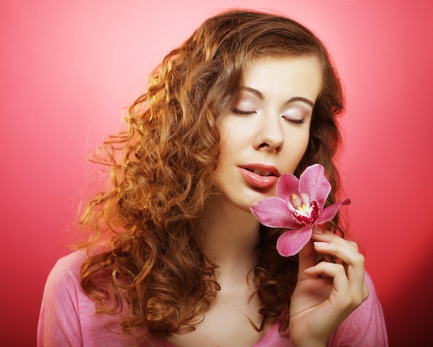 Hermosa mujer feliz con flor de orquídea sobre fondo rosa