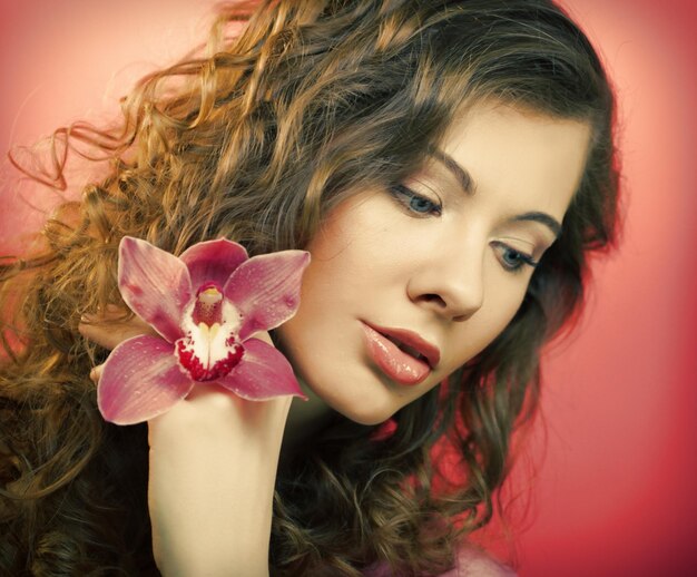 Hermosa mujer feliz con flor de orquídea sobre fondo rosa